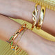 Chunky enamel-accented gold bracelet worn on model’s wrist with other bracelets
