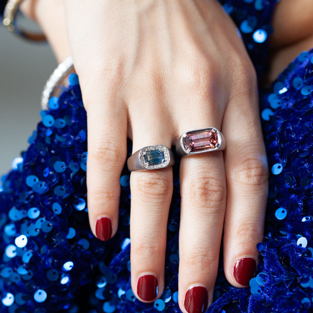 Horizontal view of 18kt white gold sapphire and diamond ring featuring emerald-cut blue sapphire and diamond halo on models hand