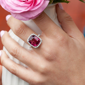 Pink tourmaline and diamond halo ring worn on hand holding a flower.